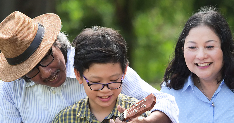 Older man and woman teaching a child to play a guitar in a park.