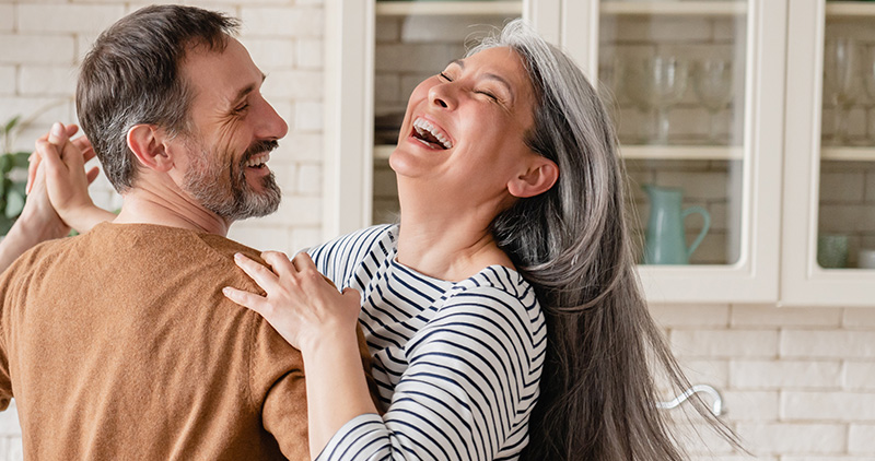 Happy middle-aged mature couple dancing together in the kitchen.