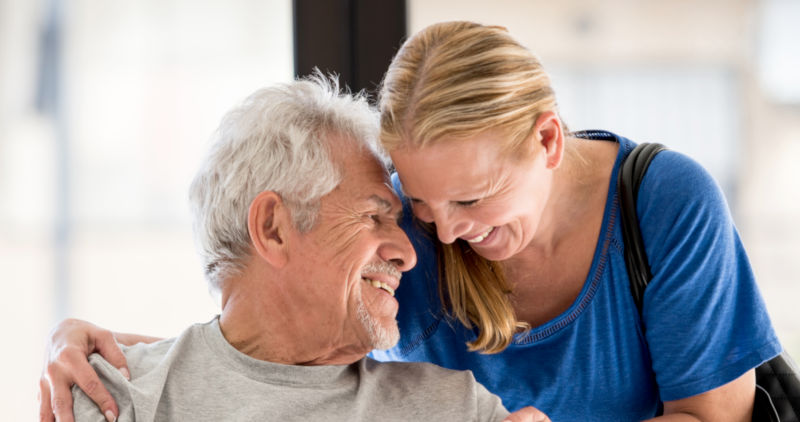 Loving couple at the doctor laughing leaning their heads together and man sitting on a wheelchair both looking happy while woman hugs him