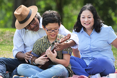 family sitting in park with son playing the ukelele