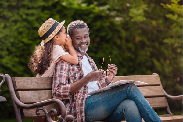 little girl in a park whispers something into her father’s ear