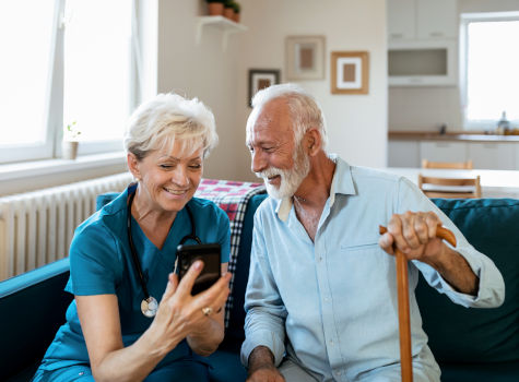A home caregiver who supports an elderly man in his home and uses a smartphone together.