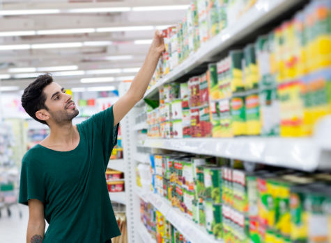 Young male taking canned food from the shelf in a store.