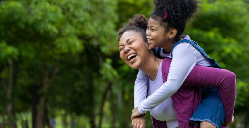 Mom giving daughter a piggyback ride outside.