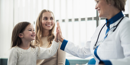 Little girl high-fiving her doctor, with mom in background