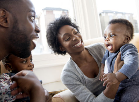 Young woman holding baby boy with man and girl looking and smiling